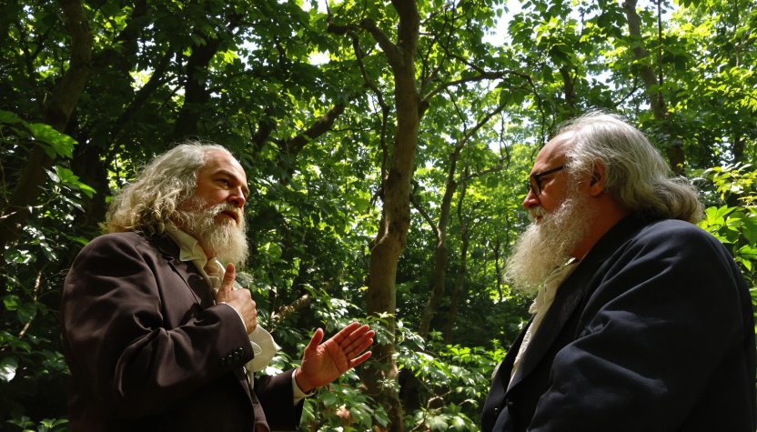 Two bearded men conversing in a forest.