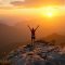 Un homme au sommet d'une montagne au coucher du soleil, les bras levés.