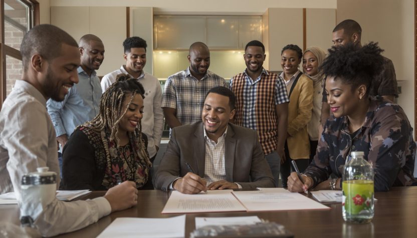 Un groupe de jeunes professionnels souriants signent des documents officiels